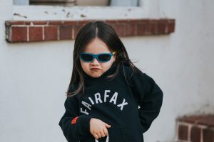 A sassy child in black fairfax sweatshirt and red sun glasses