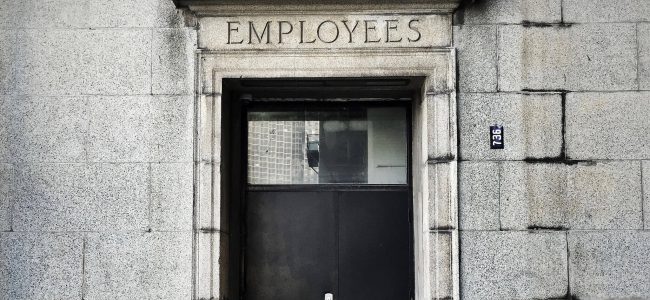 Photo of black wooden door in stone wall with employees craved into the lintal above door