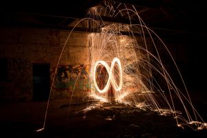 Long exposure nightime photograph of burning steel wool swung in an infinity pattern